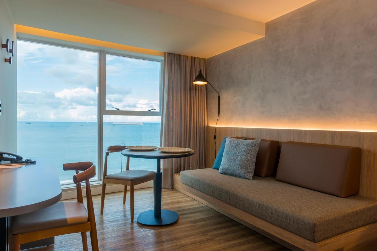 Hotel Luzeiros Fortaleza Exterior photo The photo shows a modern and stylish interior space, likely a small living area or hotel room. It features a large window with a view of the sea, allowing natural light to fill the room. There is a cozy sofa along one wall, paired with a small round 