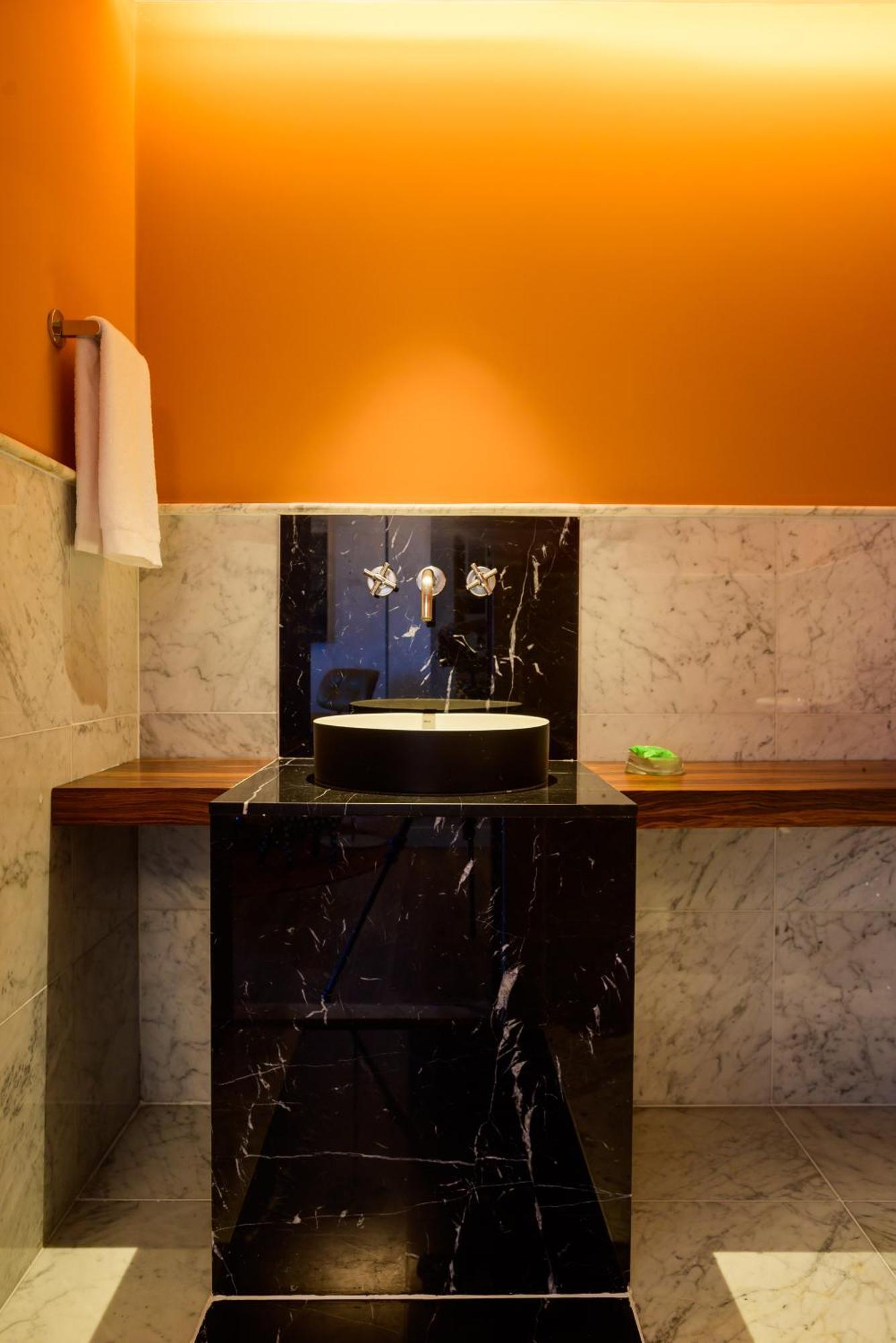 Hotel Luzeiros Fortaleza Exterior photo The photo shows a modern bathroom with a stylish design. There is a circular black sink on a dark marble base, which is complemented by a sleek, minimalist faucet with two handles. The backdrop features light-colored marble walls and a vivid orange w